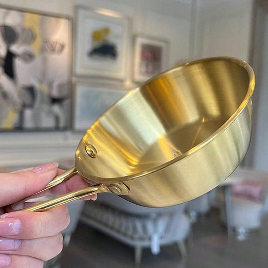 Mini stainless steel sauce pan with golden handle on stovetop